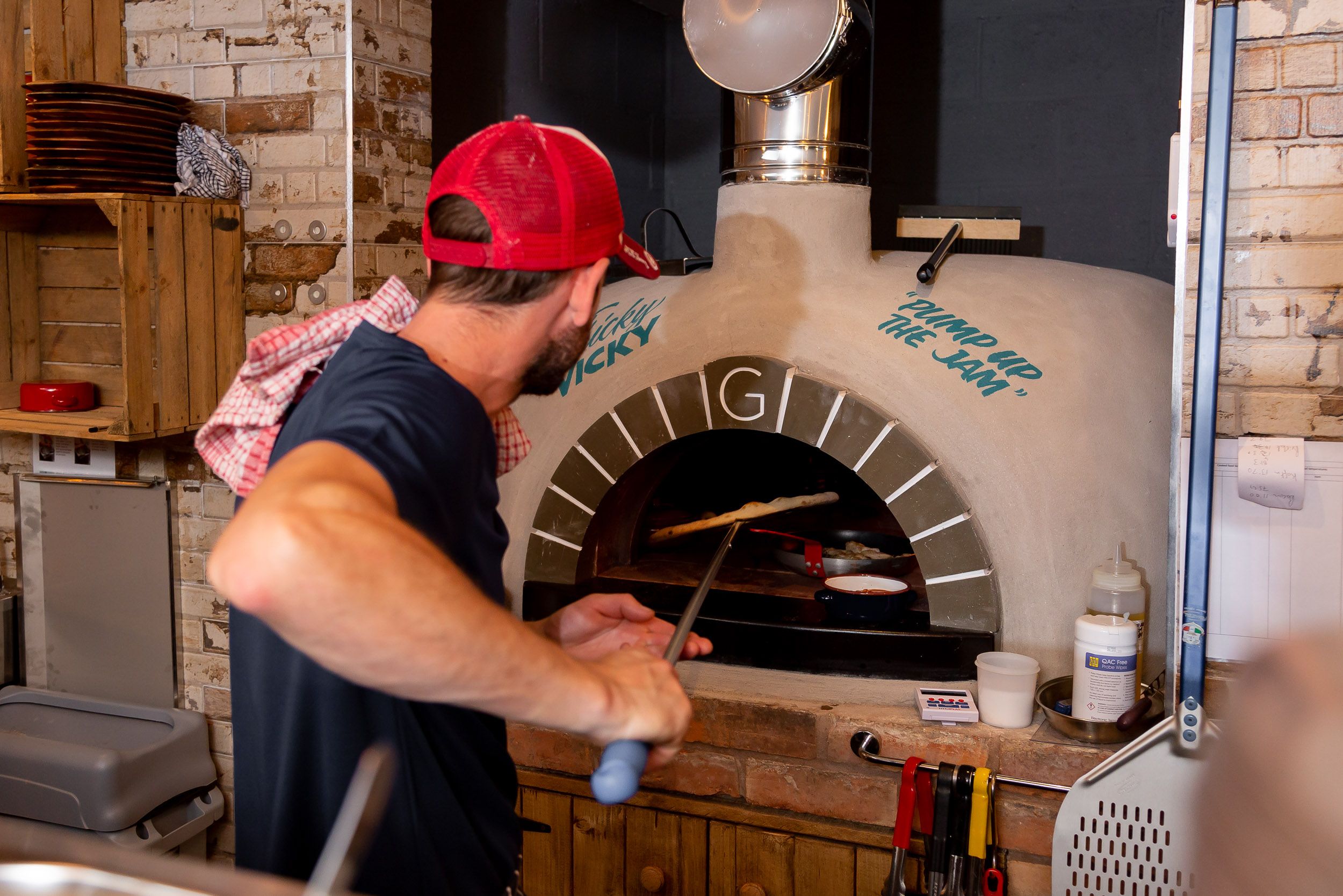 Chef weaing a red cap cooking food in pizza oven